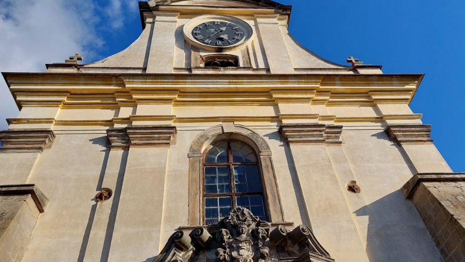 Průčelí barokního kostela v Oseku v sousedství roubené šestiboké zvonice